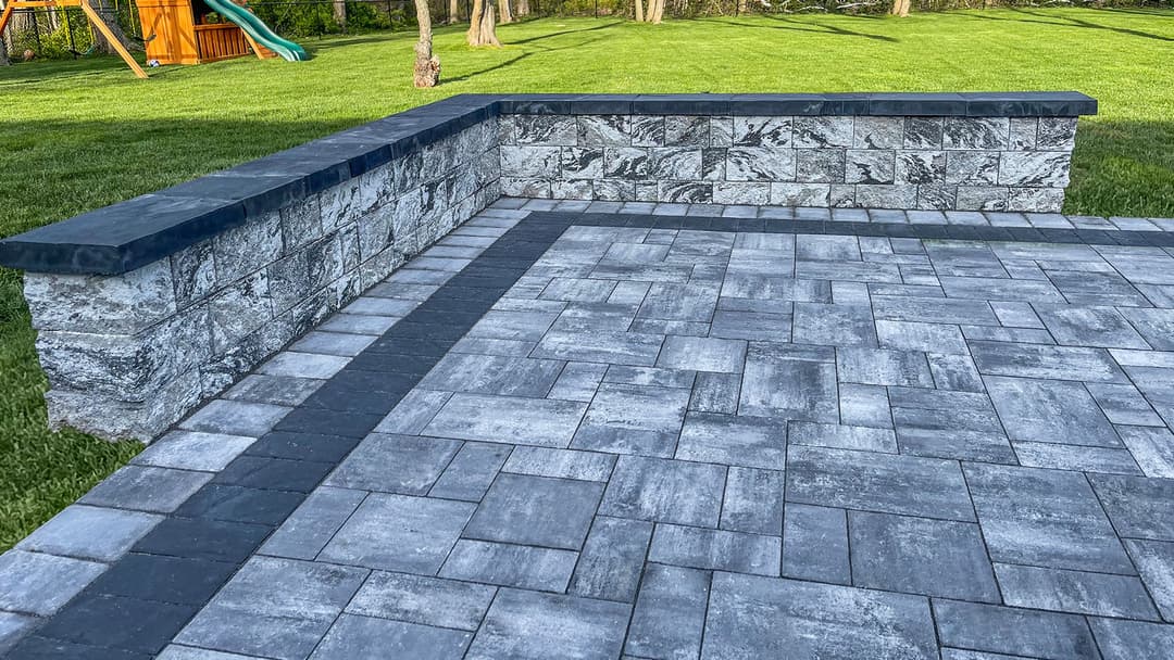 Patio featuring stone pavers and a stone wall in a green yard with a playset in the background.