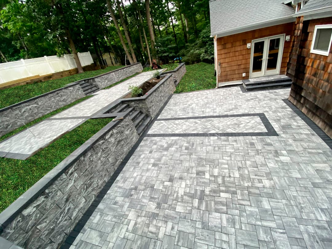 Modern backyard featuring gray paver patio, stone walls, and lush greenery in a serene setting.