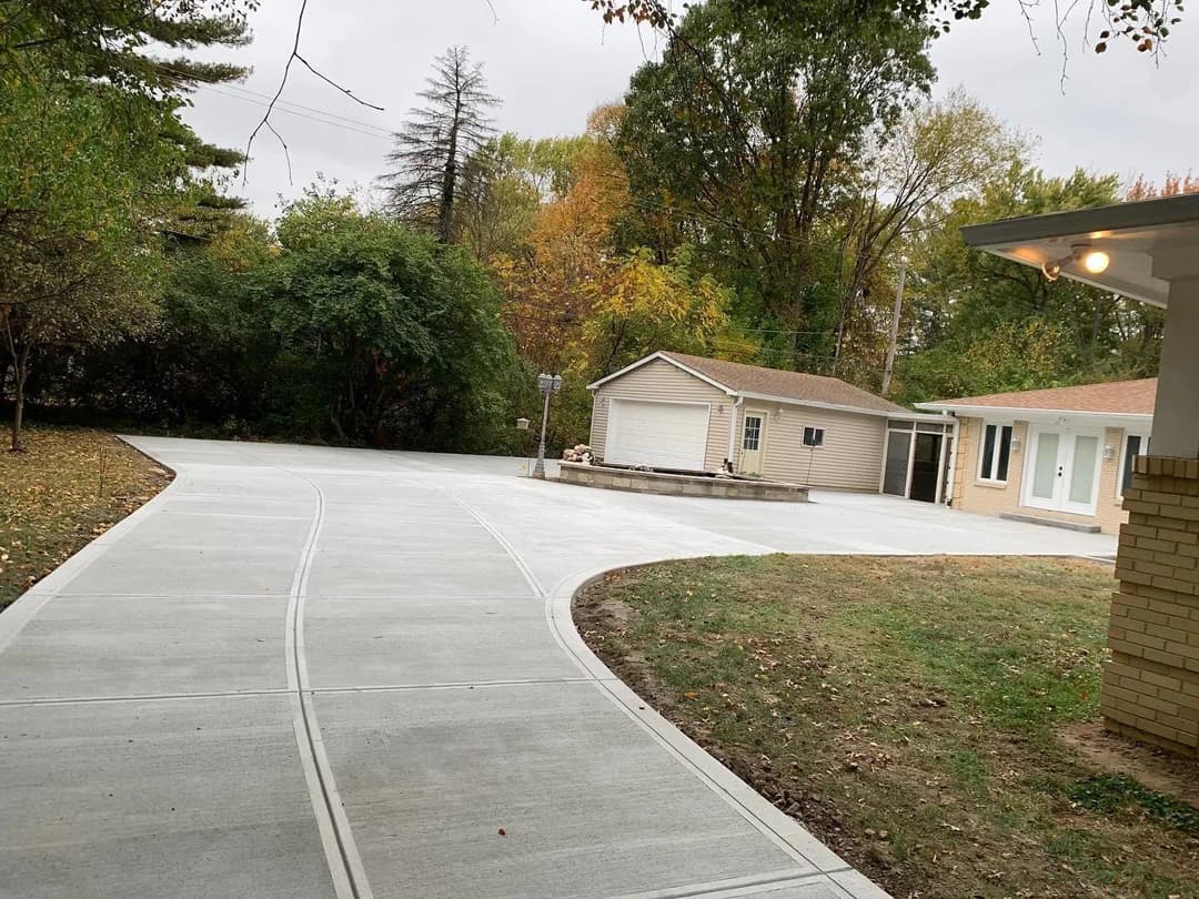 Newly poured concrete driveway leading to a home, surrounded by autumn trees and greenery.