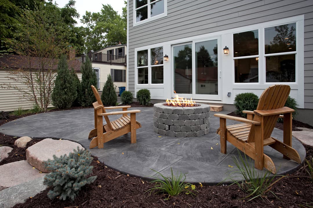 Cozy outdoor patio with fire pit, stone seating, and lush landscaping. Perfect for gatherings.