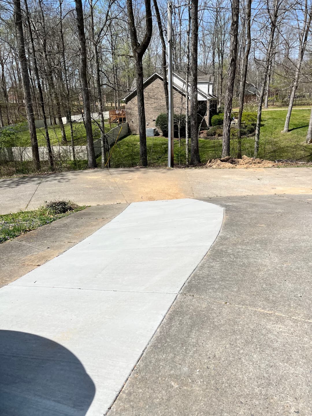 Newly poured concrete driveway leads to a house nestled among trees in a wooded area.