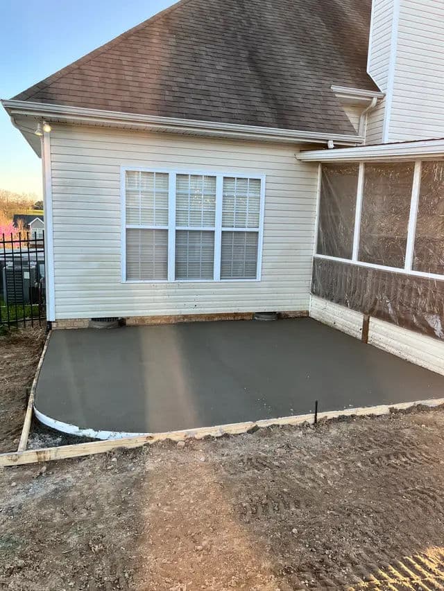 Newly poured concrete patio beside a house with a brown roof and white siding.