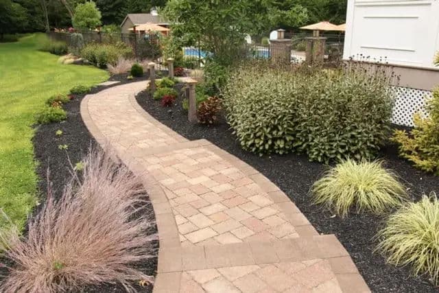 Curved stone pathway bordered by colorful plants and landscaping in a garden setting.