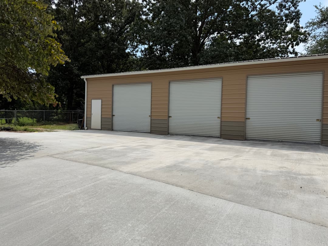 Storage facility with three large roll-up garage doors and paved driveway.