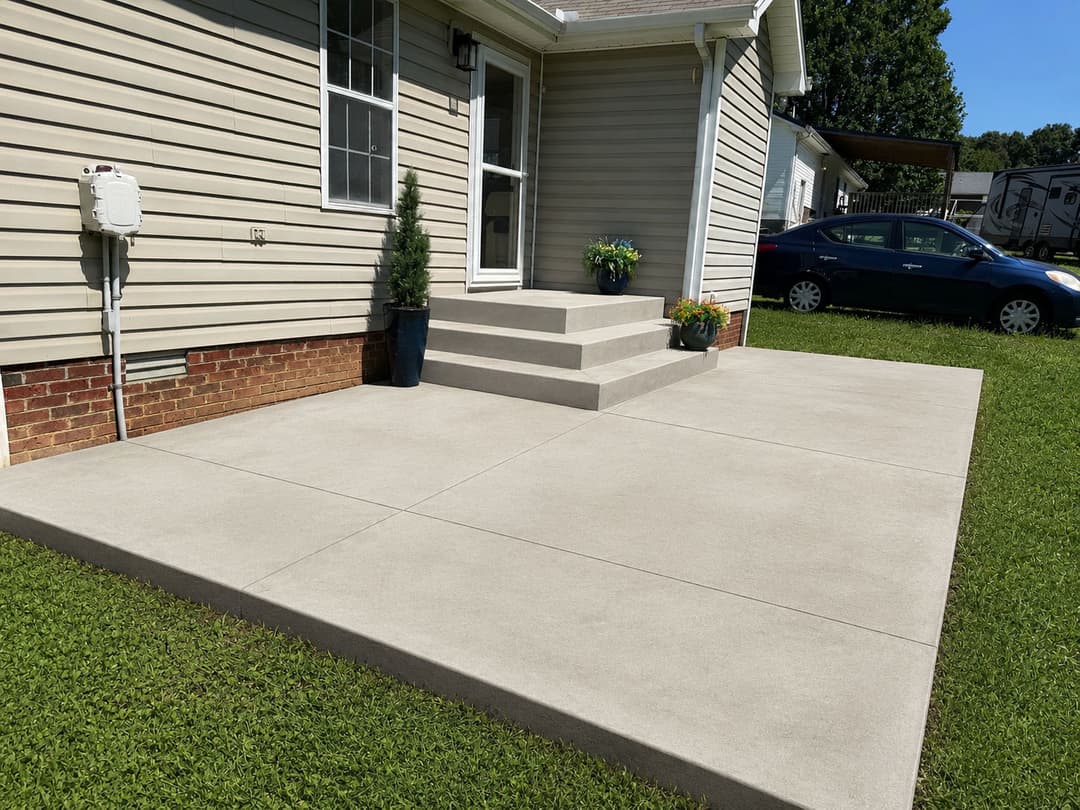 Concrete patio with steps, potted plants, and siding of a house in a suburban setting.