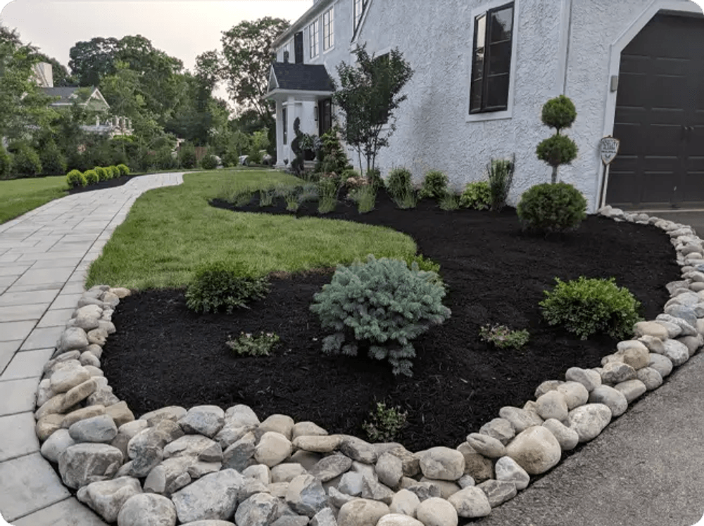 Landscape design with mulch, decorative stones, and neatly trimmed shrubs in a residential yard.